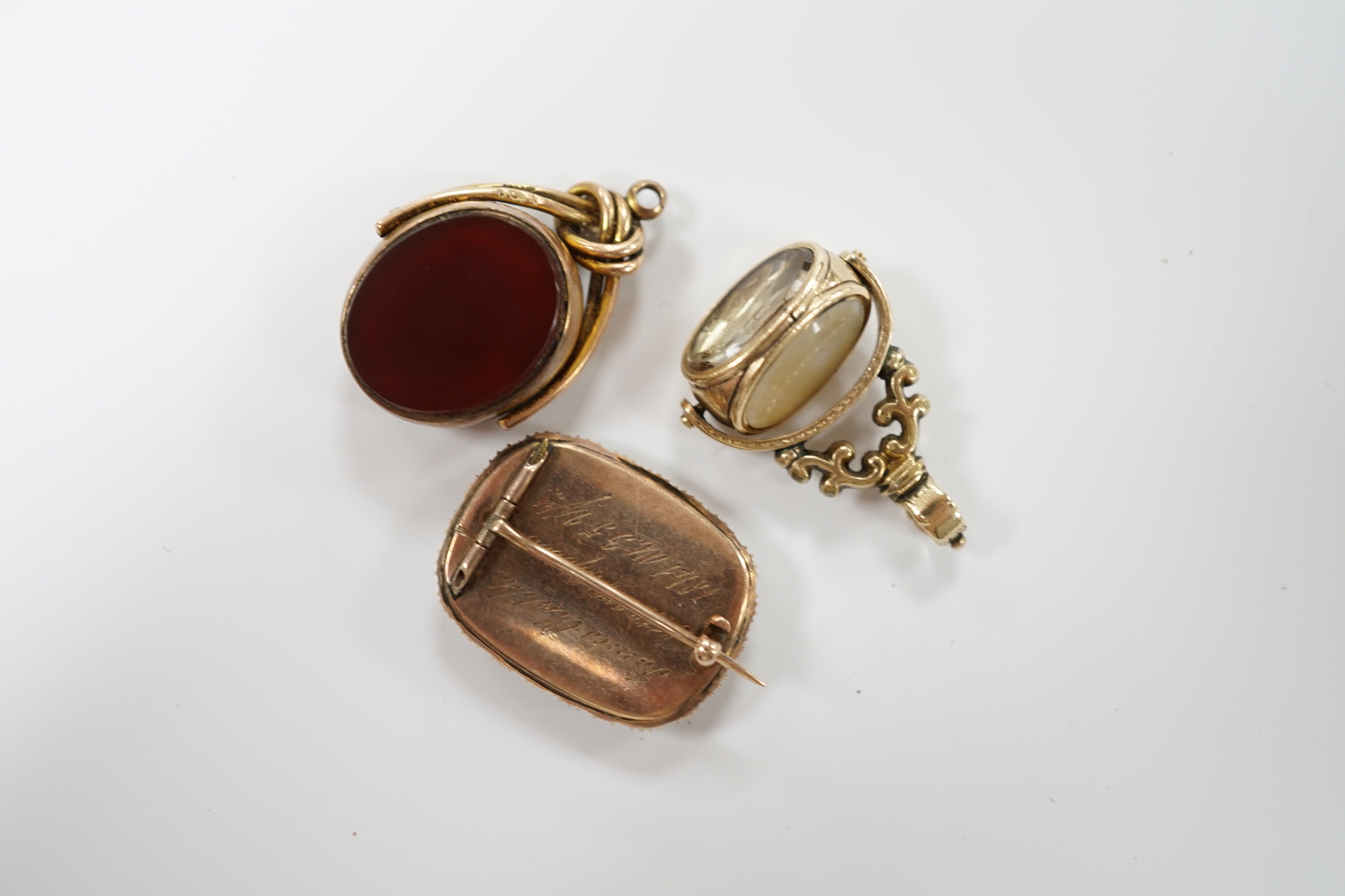 An early Victorian yellow metal and seed pearl set mourning brooch, with plaited hair, 23mm, together with two chalcedony set fob seals, including 9ct gold mounted.